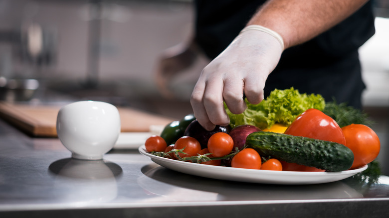 Chef using gloved hand to grab vegetables