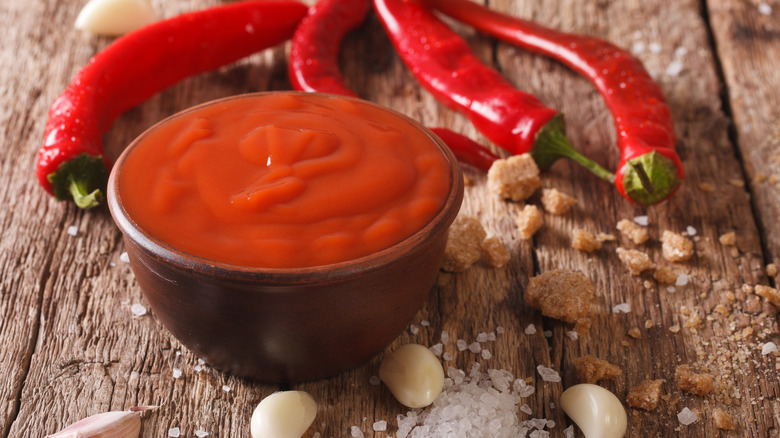 Hot sauce in a bowl with garlic, salt, peppers, and brown sugar on wood surface