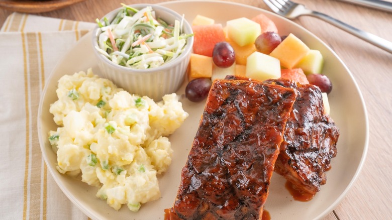 Barbecue ribs, macaroni salad, coleslaw, and fruit salad on a plate
