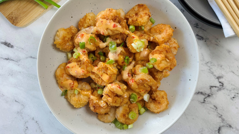 Fried shrimp in bowl topped with chili mayo sauce and scallions