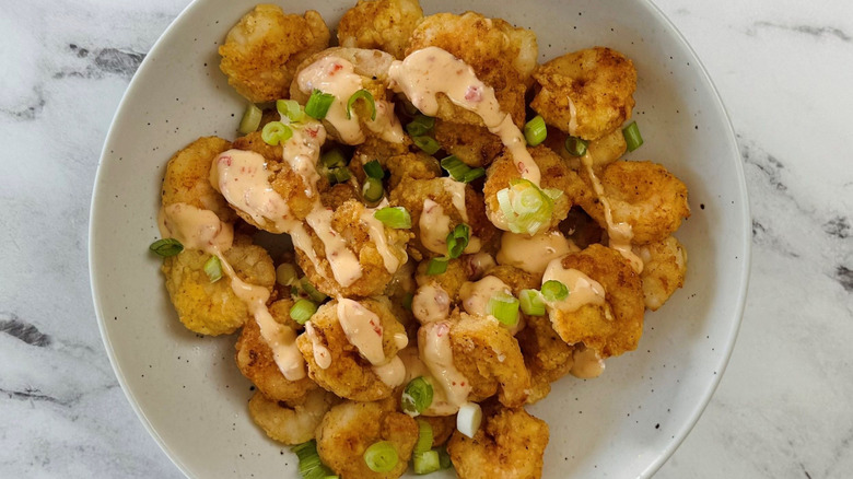 Fried shrimp in bowl drizzled with sauce and topped with scallions