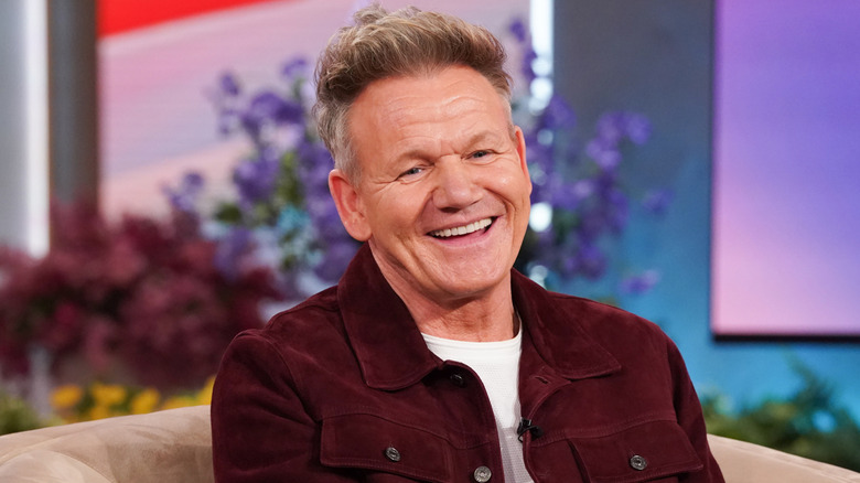 Gordan Ramsay smiling in a maroon jacket with a white shirt underneath