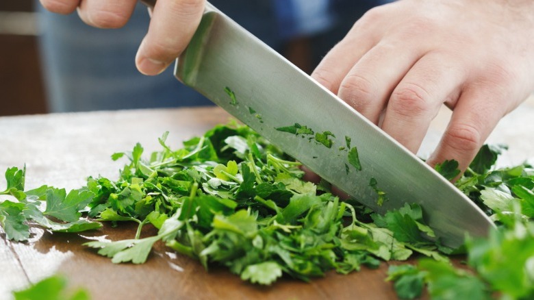 Parsley being chopped with a chef's knife on a wooden cutting board