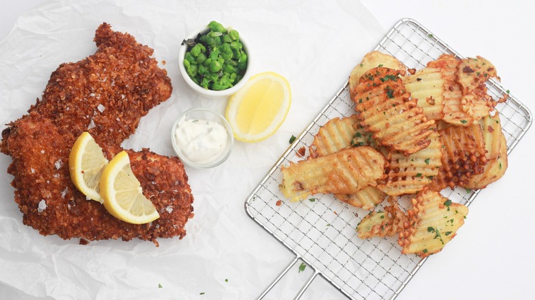 Two pieces of fried cod, mushy peas, tartar sauce, lemon slices, and waffle-cut fries