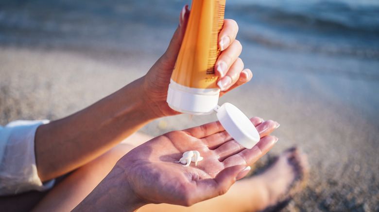 person squeezing sunscreen from a bottle beach side