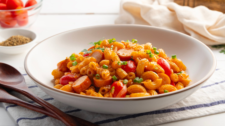 White bowl with macaroni, tomatoes, sliced hot dogs, and chives