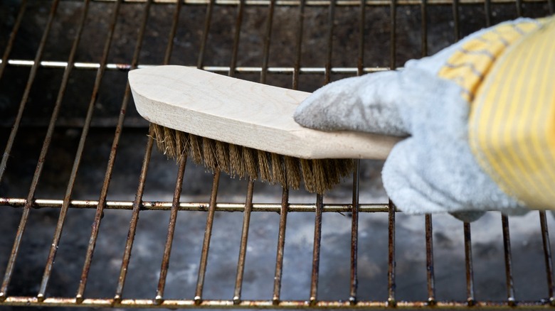 A dirty grill being scrubbed clean with a metal wire grill brush.