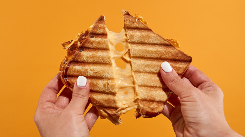 Hands pulling apart grilled cheese sandwich against orange background