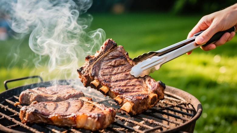 A pair of tongs is being used to flip meat on a hot grill.