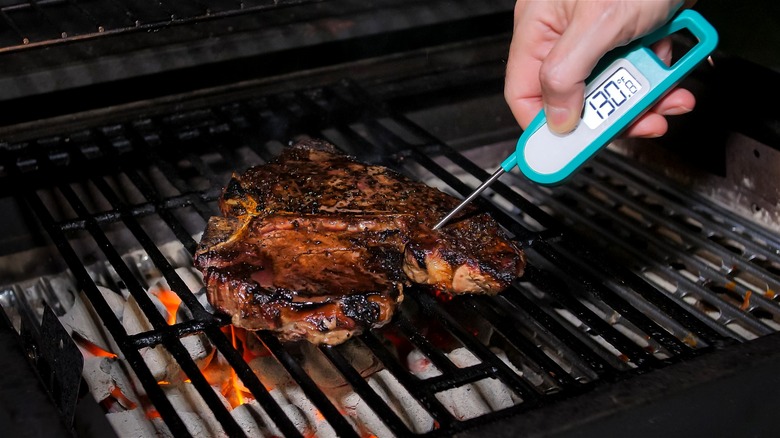 A digital thermometer is being used to check the internal temperature of meat on a grill.
