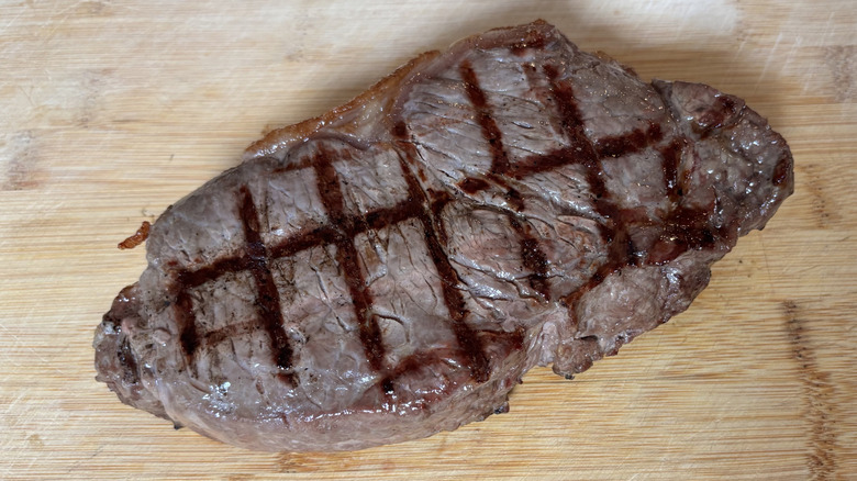 Large NY strip steak resting on a wooden cutting board after grilling