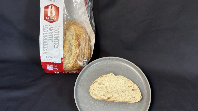 Bagged loaf of La Brea Bakery Sourdough next to slice of bread on gray plate