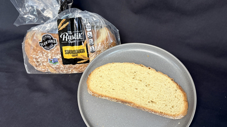 Bagged loaf of The Rustik Oven Sourdough next to slice of bread on gray plate