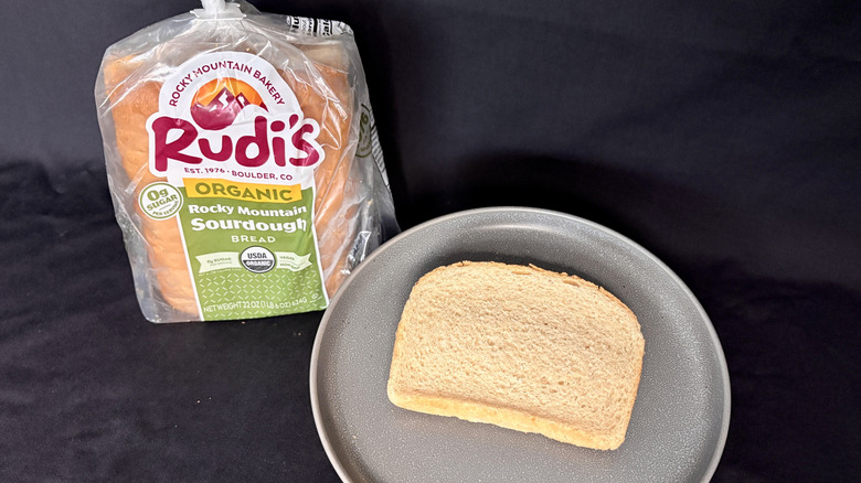 Bagged loaf of Rudi's Sourdough next to slice of bread on gray plate