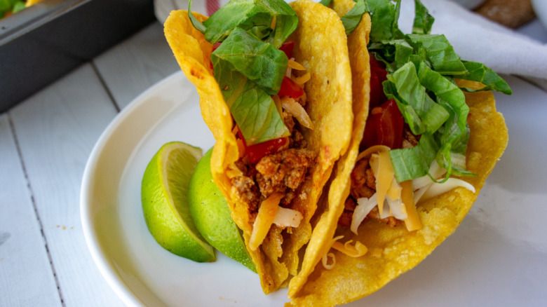 two turkey tacos on a white plate with lettuce, tomatoes, and cheese