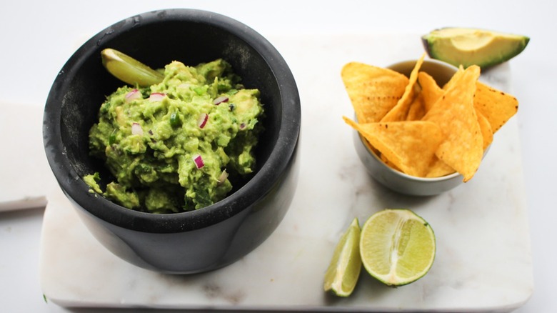 Cup of guacamole with lime wedge and tortilla chips on the side.
