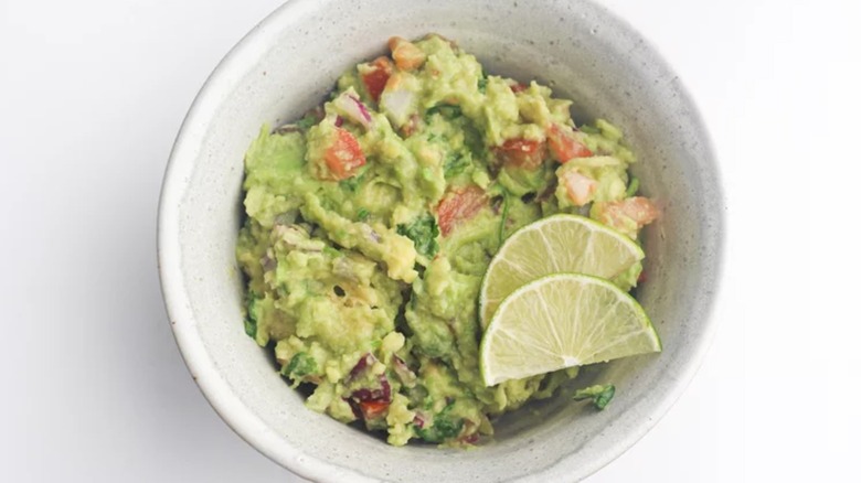 Bowl of homemade guacamole with two lime slices inside.