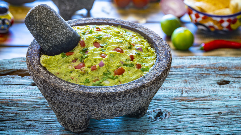 Fresh guacamole in a molcajete with ingredients in the background