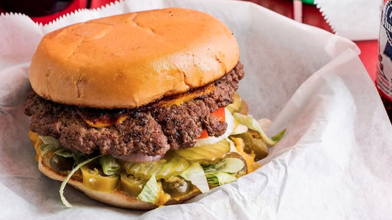 Beef burger with pickles and jalapeños on white paper