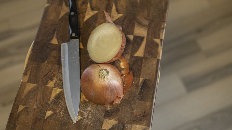 Onion cut in half and knife on wooden cutting board