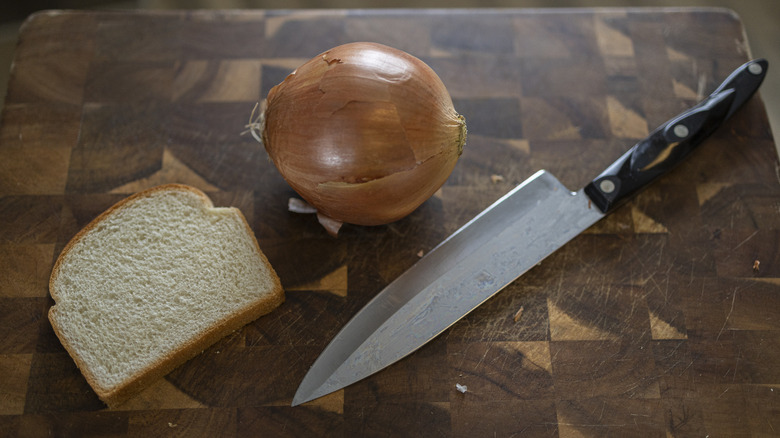 Onion, slice of bread, and knife on cutting board