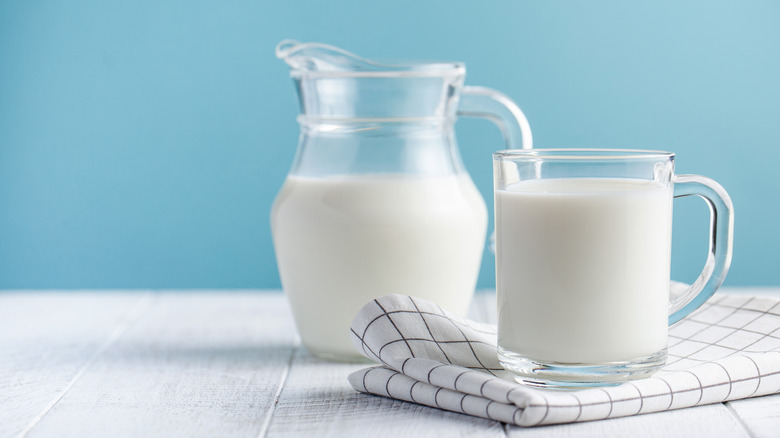 a jug of milk next to a glass of milk on a dishcloth