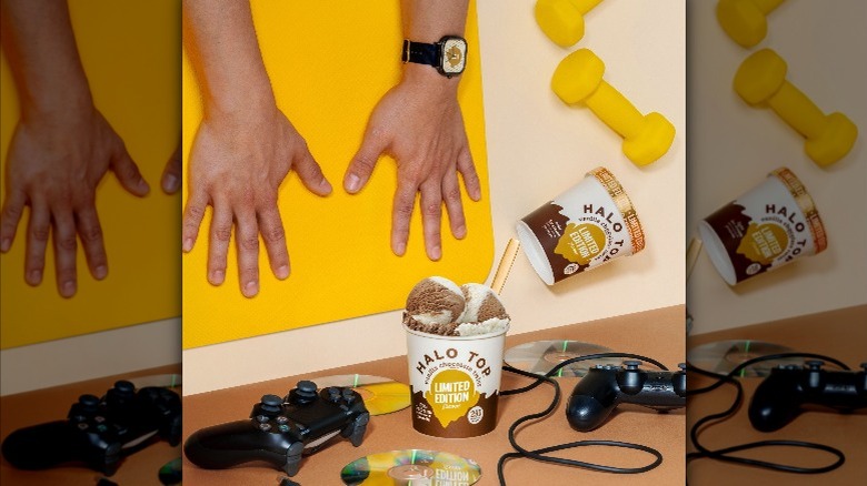 Pint of Halo Top Vanilla Chocolate Twist ice cream near gaming controls and dumb bells