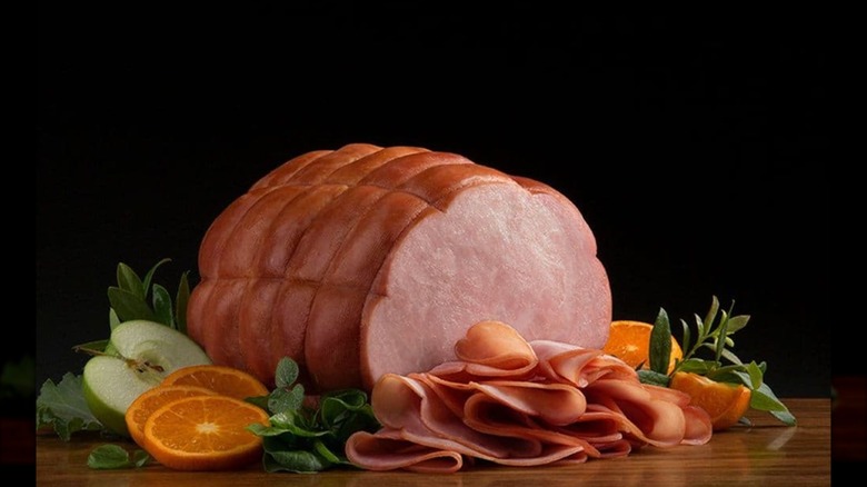 Boneless ham on a wooden countertop surrounded by apple and orange garnishes