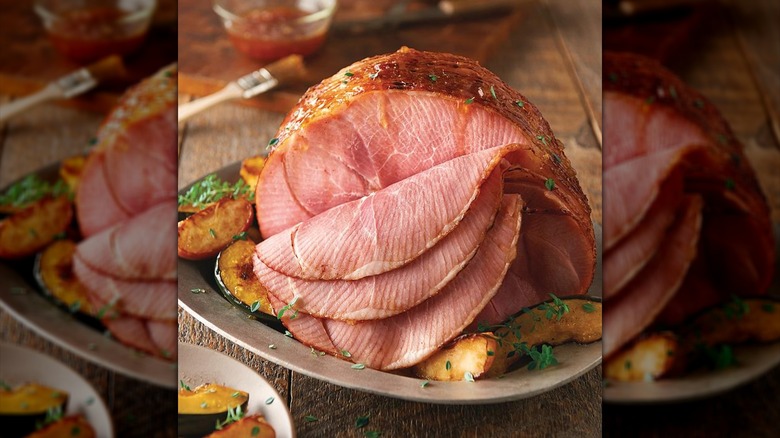 Spiral sliced ham on a serving platter surrounded by roasted vegetables