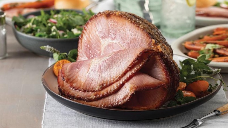 Spiral sliced ham on a black plate with a salad bowl in the background