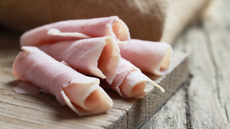 Rolled up thick ham slices on a wooden cutting board
