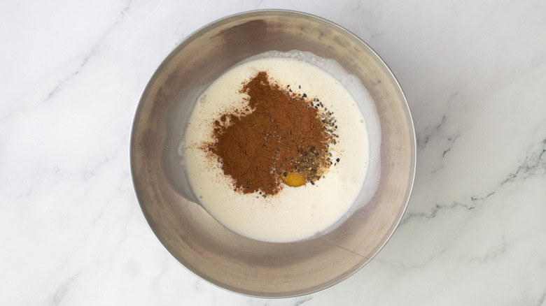 Heavy cream, eggs, cinnamon, and black pepper in mixing bowl