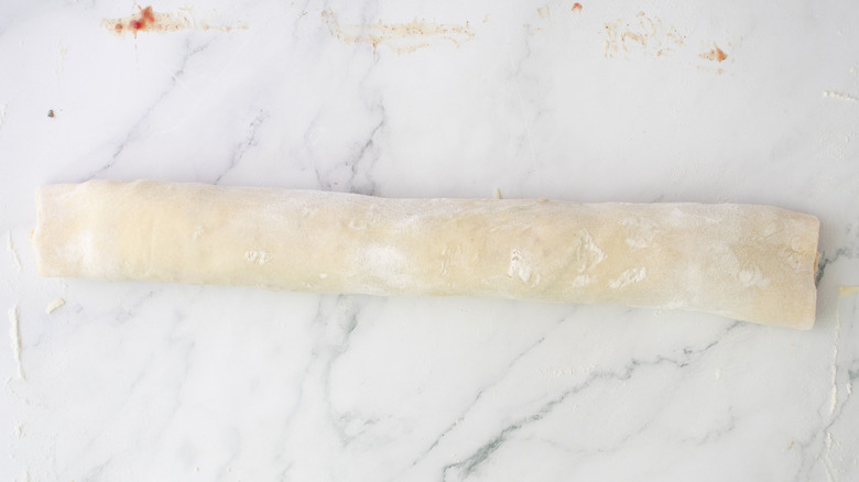 Stuffed puff pastry rolled up into a log on a marble surface