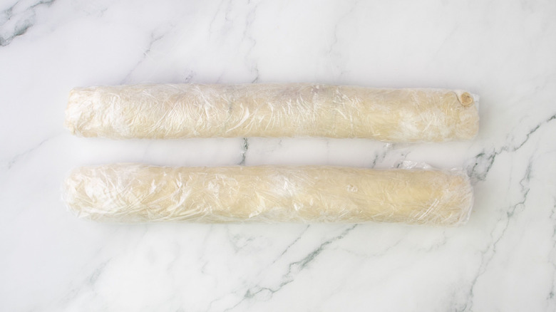 Puff pastry logs wrapped in plastic wrap on marble surface