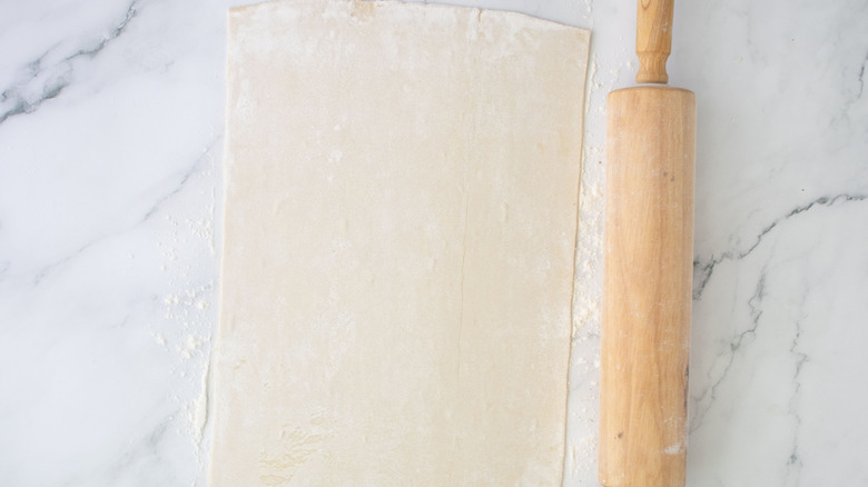 Puff pastry sheet rolled out on marble surface next to rolling pin
