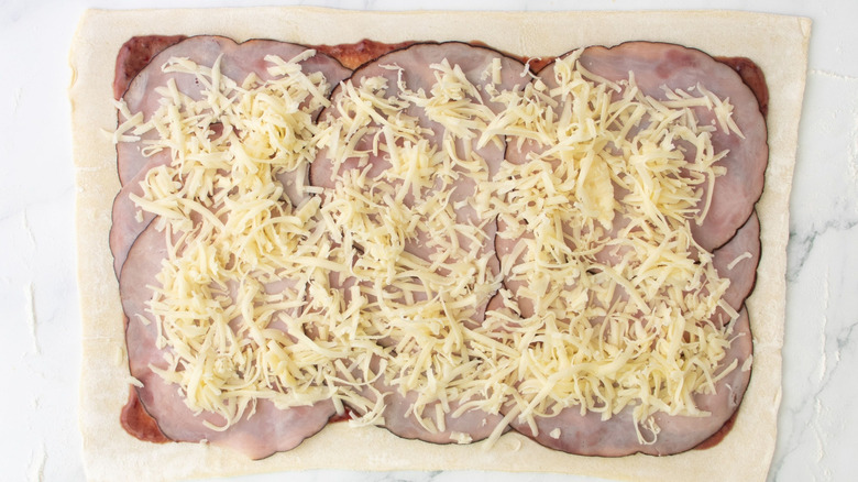 Puff pastry sheet layered with jam, ham slices, and Gruyère cheese