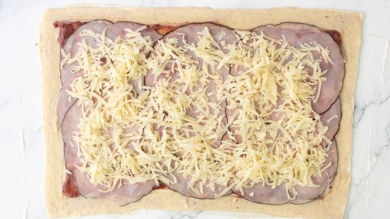 Puff pastry sheet brushed with egg wash and layered with jam, ham slices, and Gruyère cheese