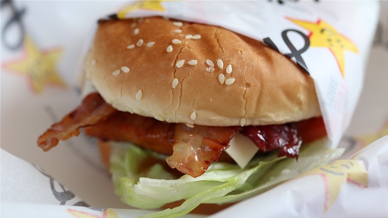 close up of carl's jr. burger with bacon and lettuce, bun topped with sesame seeds