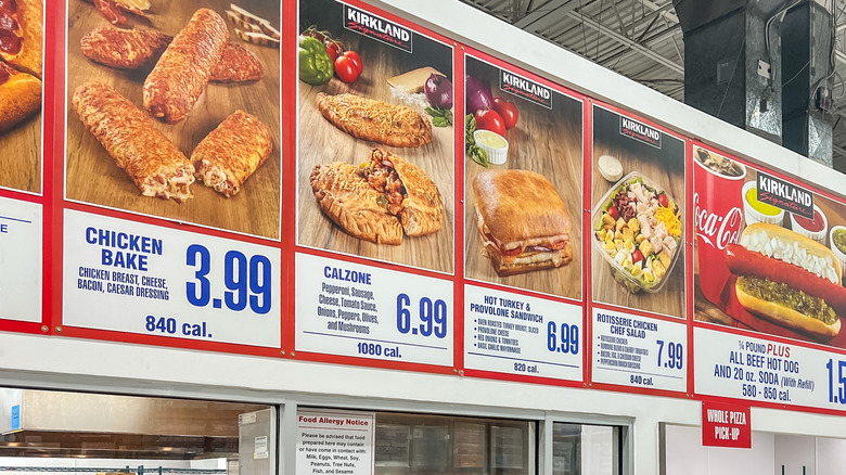 Costco menu board showing the chicken bake, calzone, turkey and provolone sandwich, rotisserie chicken salad, and Kirkland beef hotdog