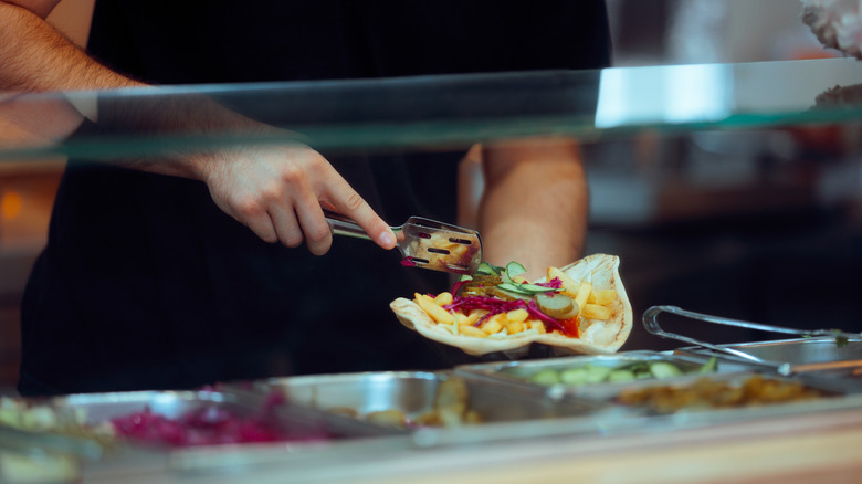 A man assembling a tortilla wrap behind the counter