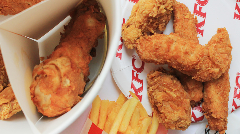A bucket of KFC chicken tenders and chicken wings with some fries