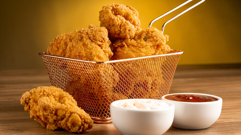 Fry basket full of fried chicken with white cups of ketchup and mayo.