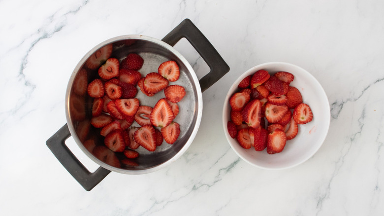 Sliced strawberries in pot next to strawberries in bowl