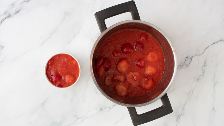 Small bowl of strawberry pie filling next to pot with strawberry pie filling