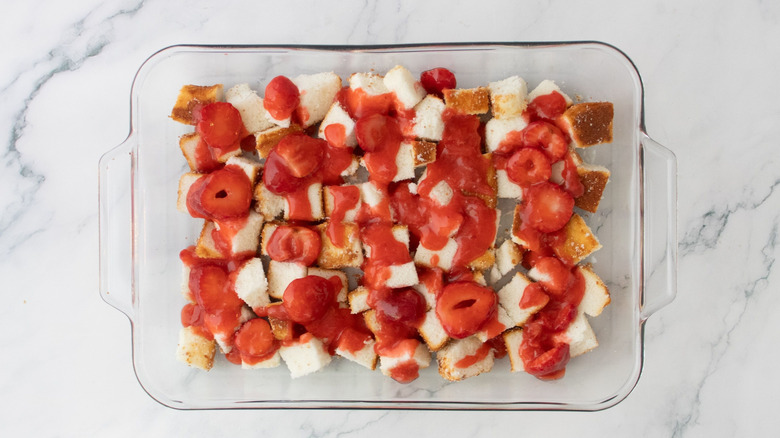 Strawberry filling drizzled over angel food cake cubes in baking dish