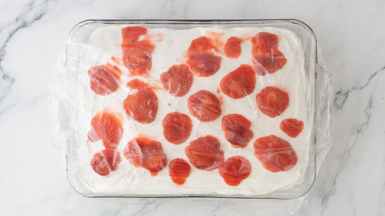 Strawberry-topped cake covered with plastic wrap in baking dish