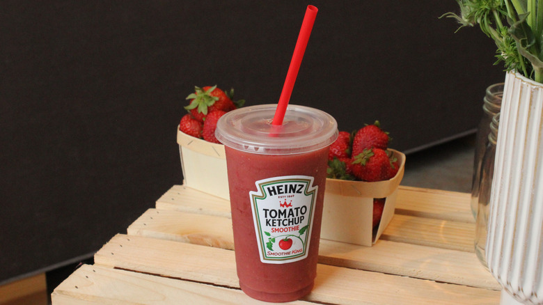 Heinz tomato ketchup smoothie with a red straw, next to some baskets of strawberries