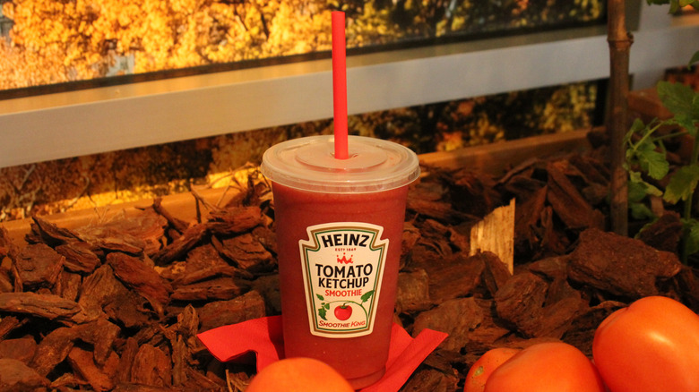 Heinz tomato smoothie in a cup standing among wood chips and tomatoes