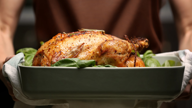 Woman holding roasted turkey in pan over bed of greens
