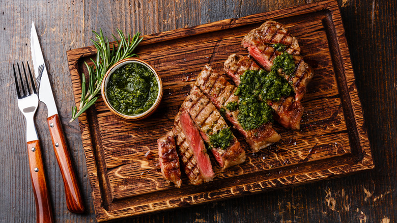 Steak on grooved cutting board with chimichurri